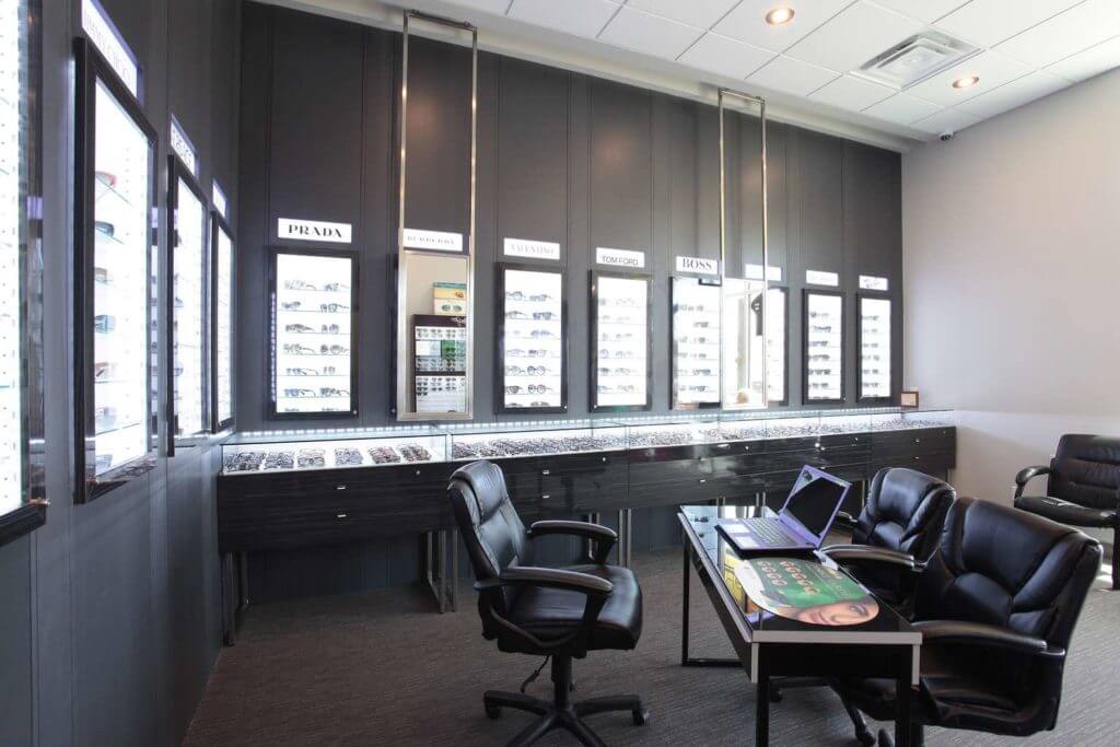 Optical store with with dark cabinets, suspended mirrors and leather chairs.