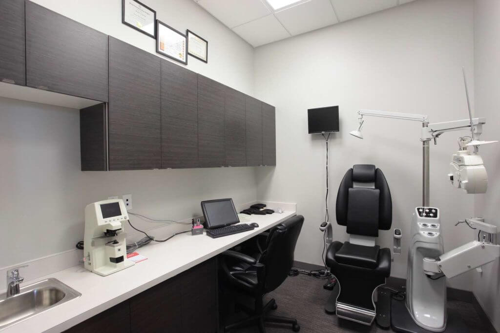 Optical treatment room with built-in dark cabinetry, white counters and medical equipment.