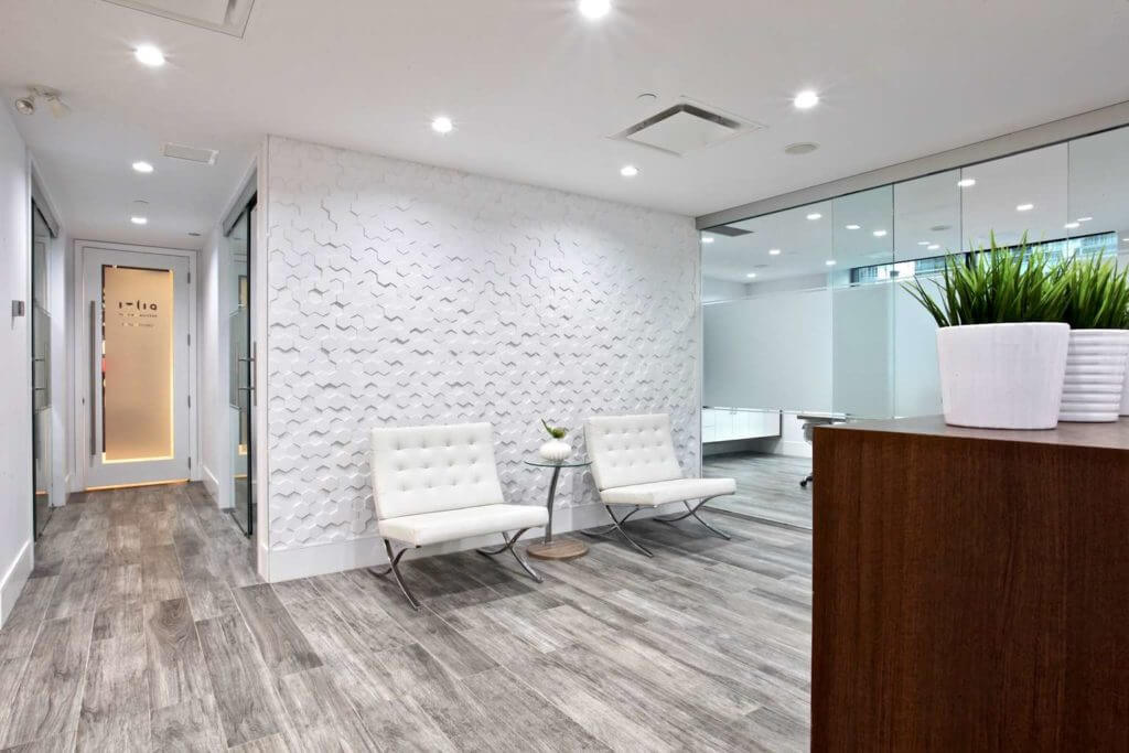 Reception area in a corporate downtown office with textured hexagonal wall panels and white leather barcelona chairs.