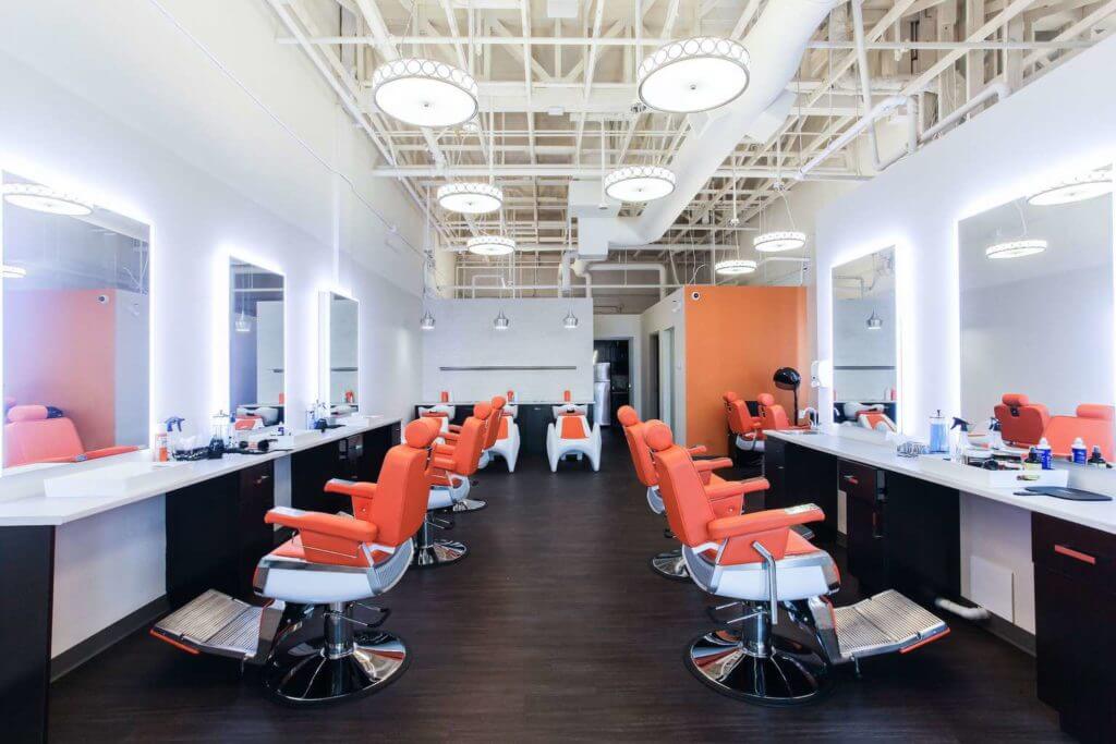 Interior of the chic beauty saloon with open ceiling, dark vinyl plank floor and orange saloon chairs.