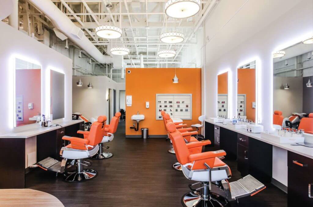 Interior of chic beauty saloon with dark vinyl plank floor, open ceiling and orange leather saloon chairs.