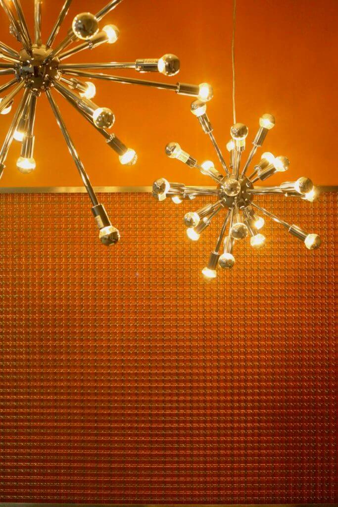 Orange accent wall with decorative cooper panels and the futuristic chandelier.